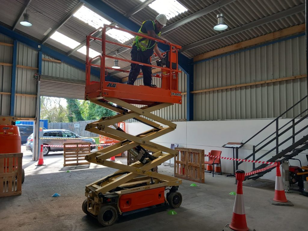 Worker on scissor lift in indoor warehouse.