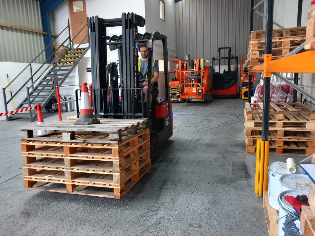 Worker operating forklift in warehouse with pallets.
